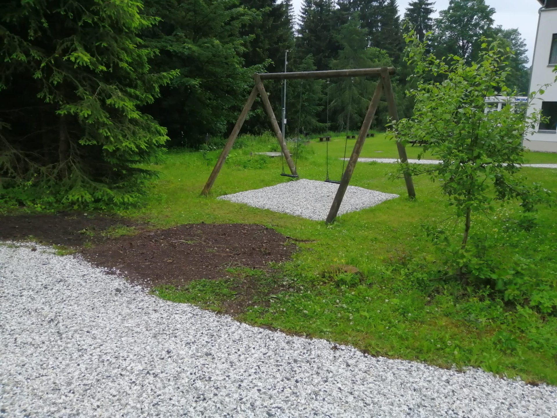 Gartenbereich mit Holzschaukel, Kiesfläche und frischem Rasen